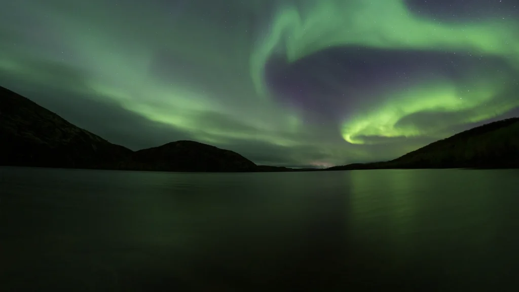 Aurora boreal verde sobre un lago rodeado de montañas en Islandia