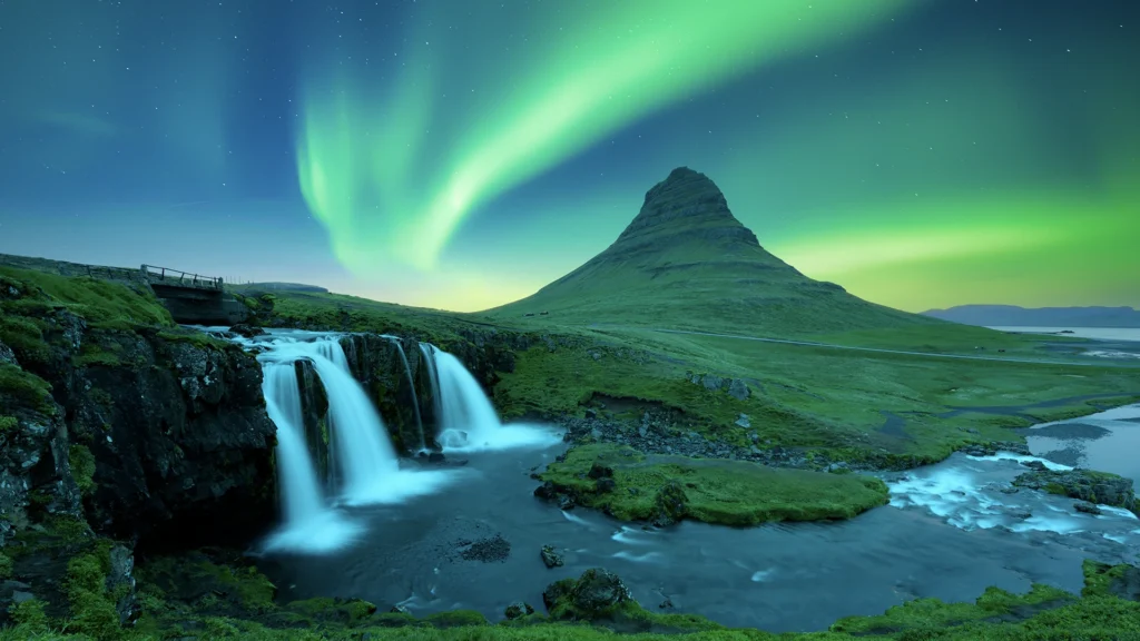 Aurora boreal verde sobre una montaña junto a una cascada en Islandia
