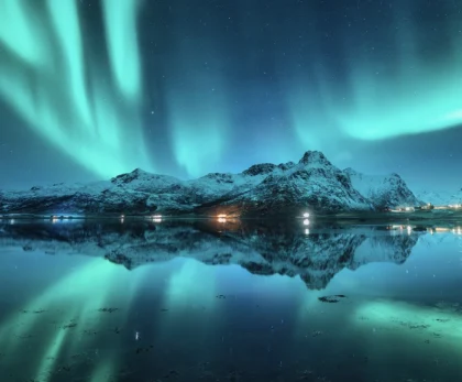 Aurora boreal verde reflejada en el agua frente a montañas nevadas de Islandia
