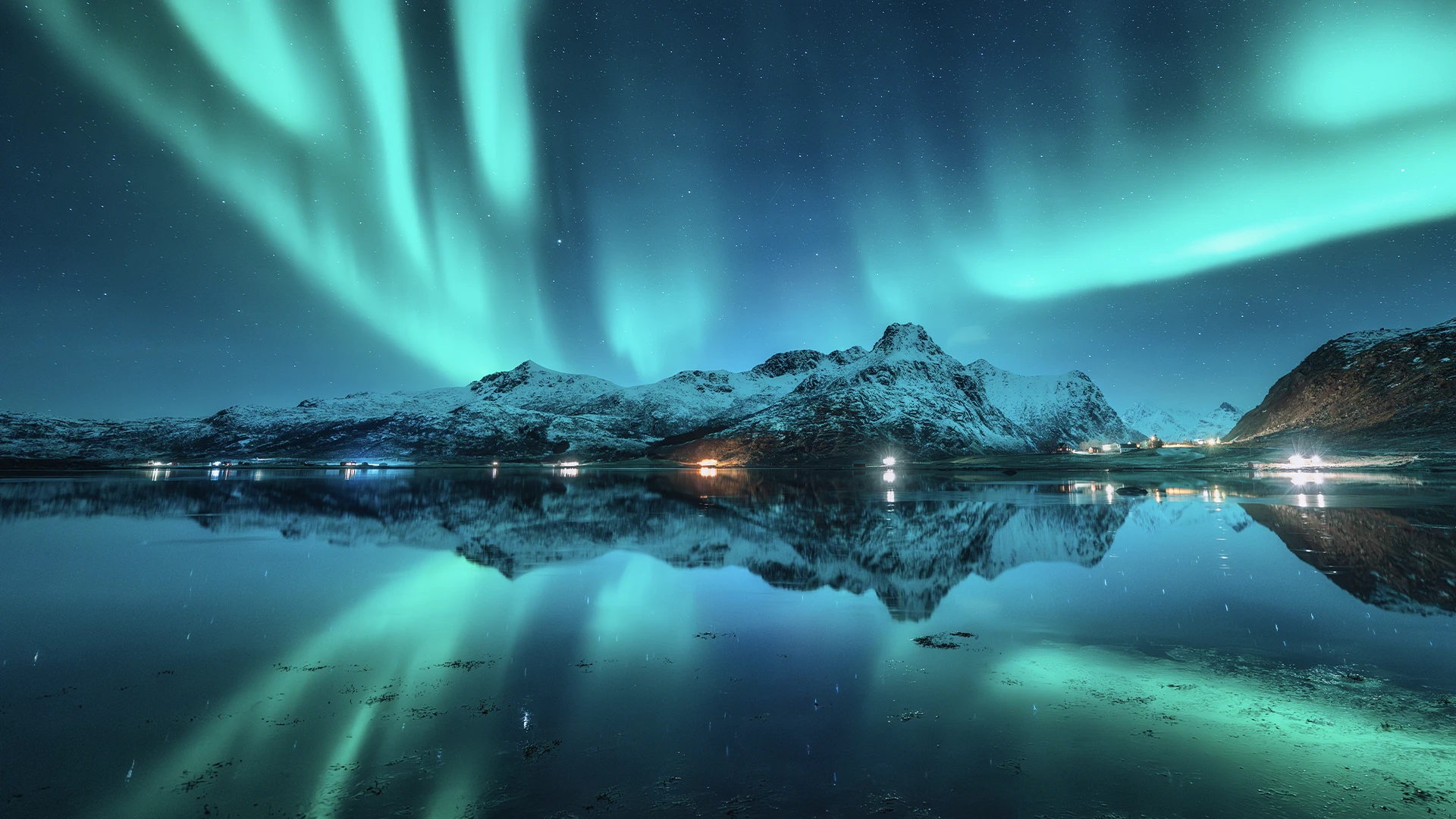 Aurora boreal verde reflejada en el agua frente a montañas nevadas de Islandia