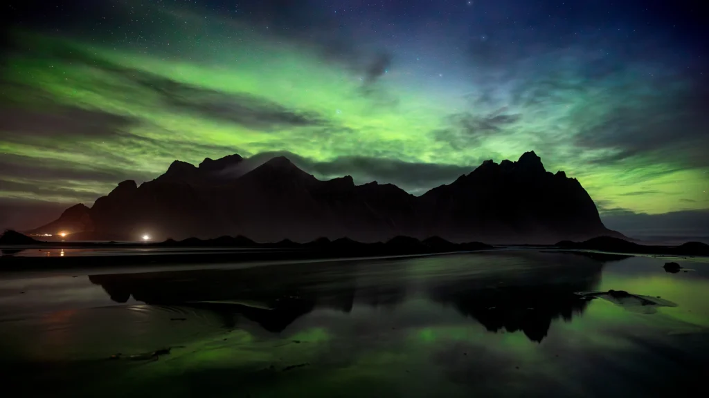 Aurora boreal verde sobre montañas oscuras reflejadas en el agua en Islandia