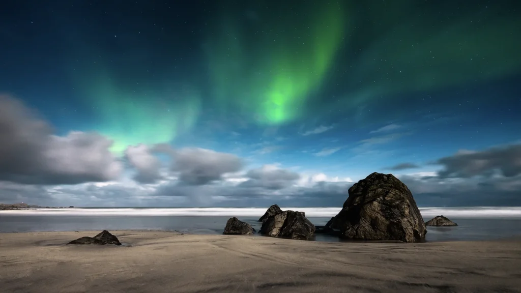 Aurora boreal verde sobre una playa de Islandia con grandes formaciones rocosas junto al mar