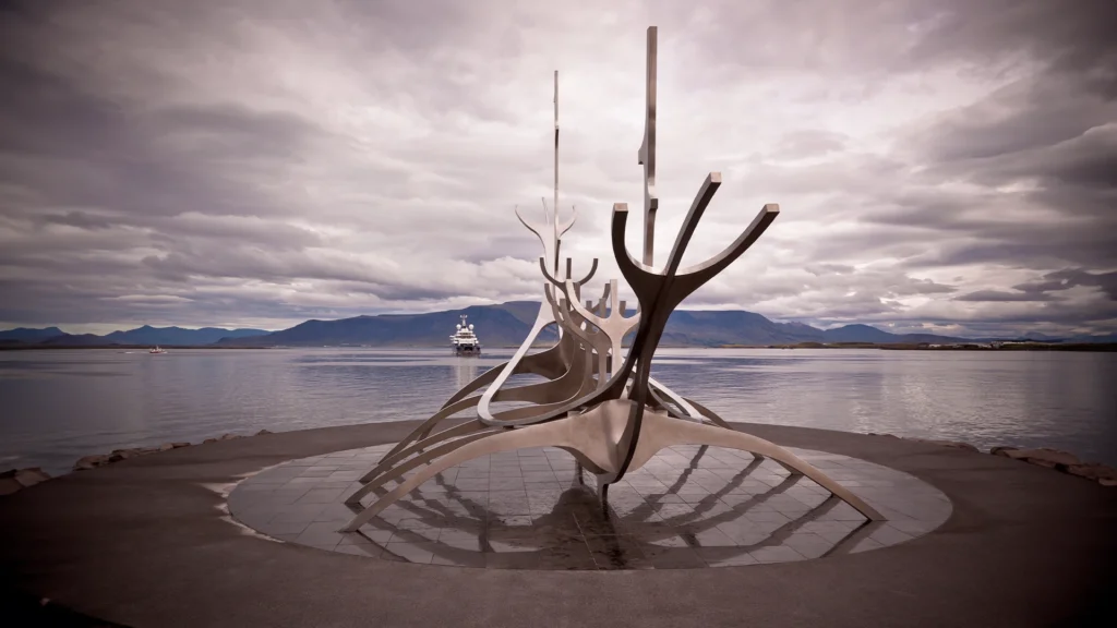 Escultura Viajero del Sol frente al mar y las montañas de Reikiavik, Islandia, bajo un cielo nublado.