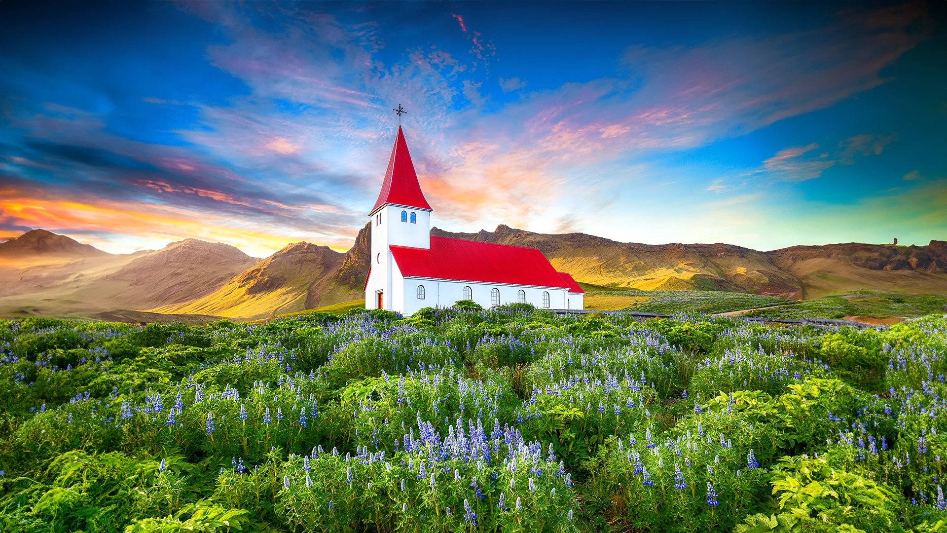 Iglesia Víkurkirkja rodeada de flores y montañas durante el atardecer en Vík, Islandia.
