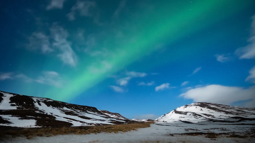 Aurora boreal verde sobre montañas nevadas bajo el cielo nocturno de Islandia.