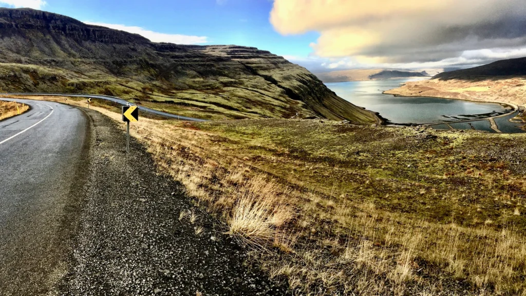 Carretera sinuosa entre montañas y un fiordo de Islandia, rodeada de vegetación otoñal.