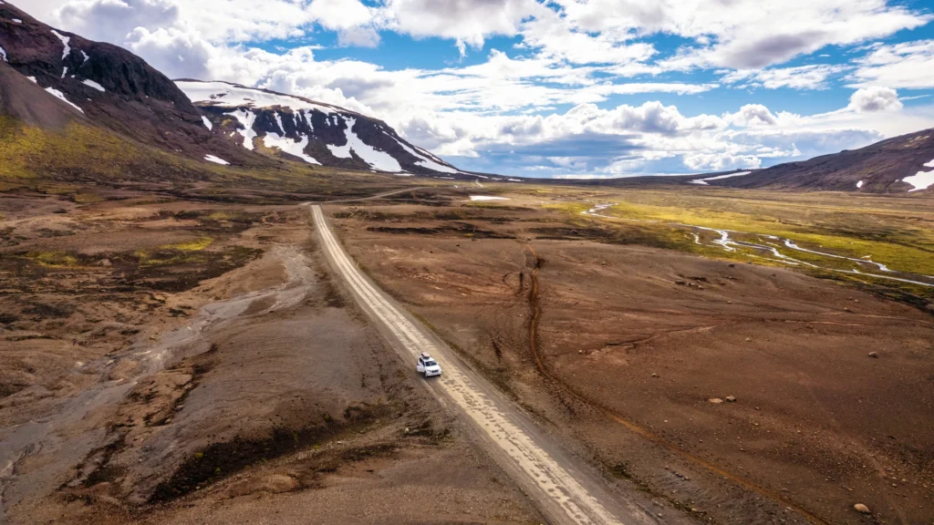 Coche recorriendo una carretera de las Tierras Altas de Islandia entre montañas nevadas