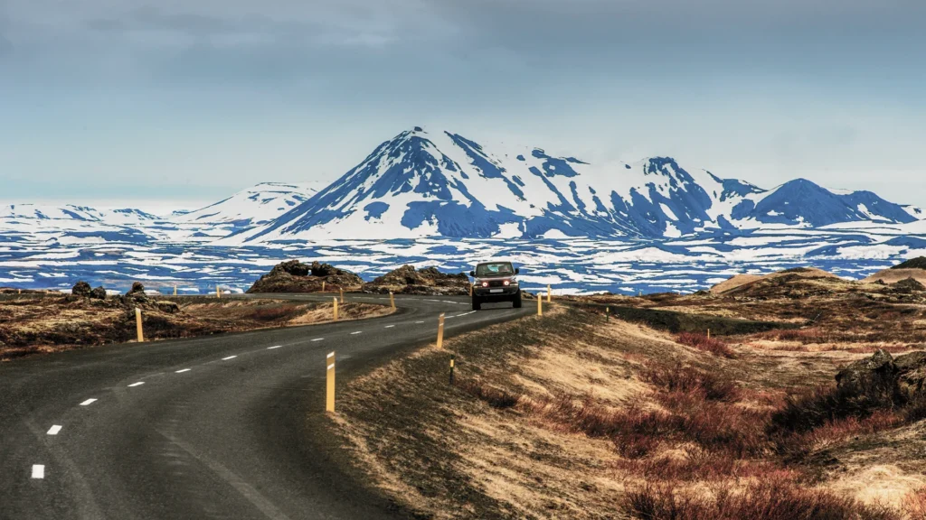 Coche recorriendo una carretera de Islandia con montañas nevadas al fondo