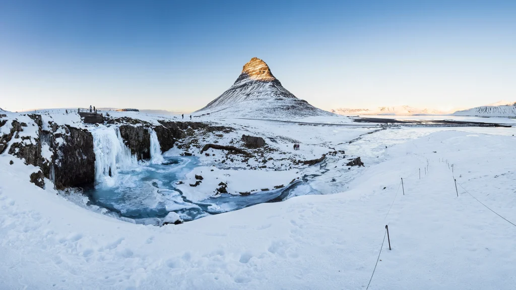 Kirkjufell y la cascada Kirkjufellsfoss cubiertos de nieve al atardecer, en la península de Snæfellsnes.