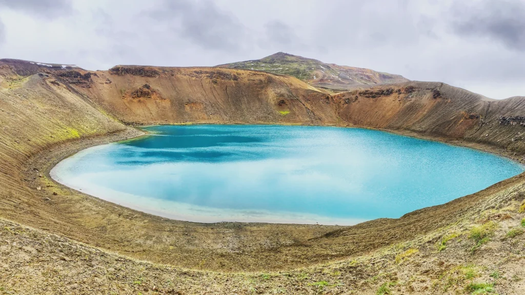 Lago azul turquesa del cráter Víti en Krafla rodeado de laderas volcánicas en Islandia