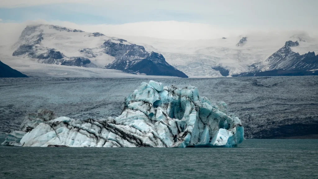 Bloque de hielo azul flotando en la laguna glaciar de Jökulsárlón, con montañas nevadas al fondo.
