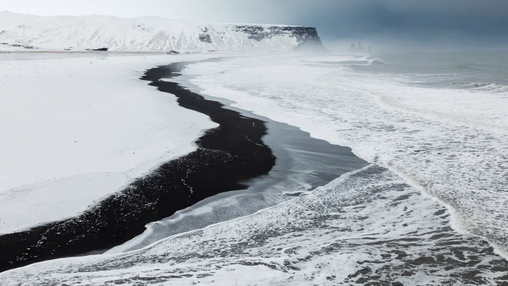 Playa de arena negra en Islandia con montañas nevadas al fondo.