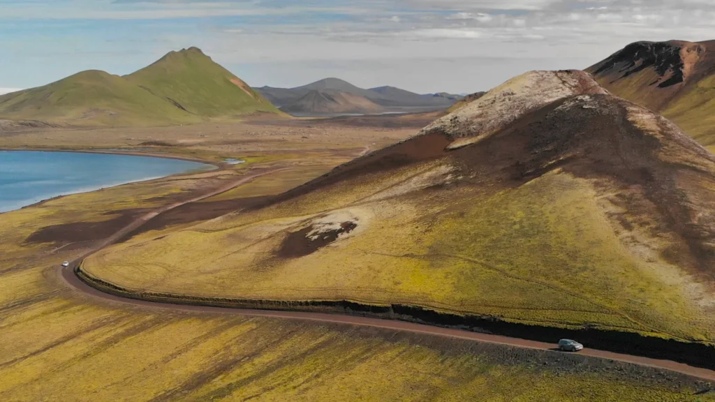 Coche recorriendo una carretera entre montañas volcánicas y un lago en Islandia