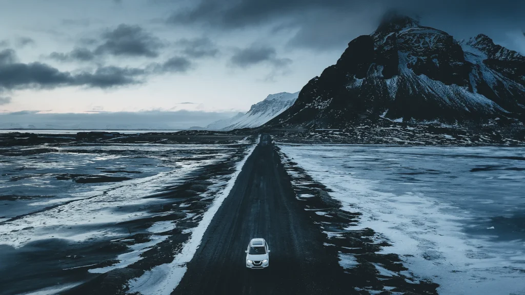 Coche circulando por una carretera nevada de Islandia entre montañas en invierno