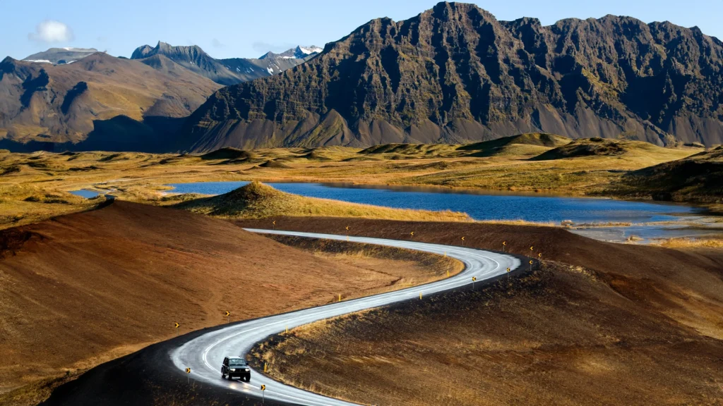 Coche recorriendo una carretera entre montañas y paisajes volcánicos de Islandia