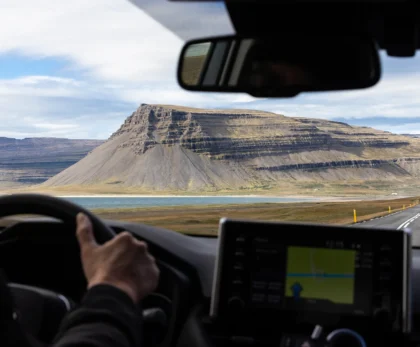 Conducción por una carretera de Islandia vista desde el interior de un coche de alquiler, con montañas y un fiordo al fondo.