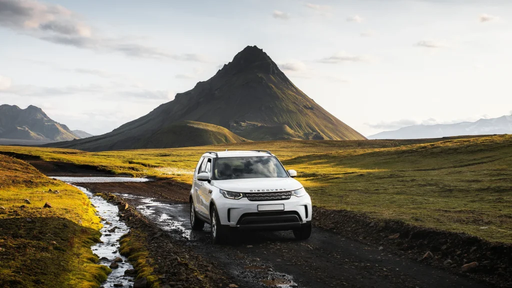 Todoterreno blanco Land Rover Discovery en un camino de grava de Islandia, rodeado de montañas y praderas verdes.