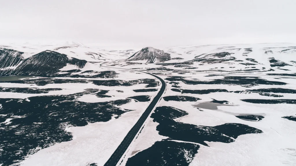 Carretera asfaltada que atraviesa un paisaje de montañas cubiertas de nieve en Islandia, vista desde el aire.