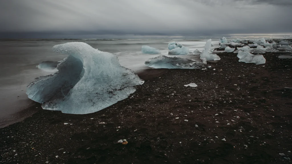 Bloques de hielo glaciar sobre la arena negra de Diamond Beach, en Islandia, junto al océano Atlántico y bajo un cielo nublado.