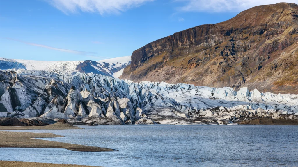 Glaciar de Skaftafell con una laguna en primer plano y una montaña rocosa al fondo.