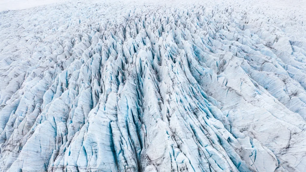 Vista aérea de la superficie de un glaciar en Islandia, con profundas grietas, crestas de hielo blanco y azul y numerosas formaciones glaciares.