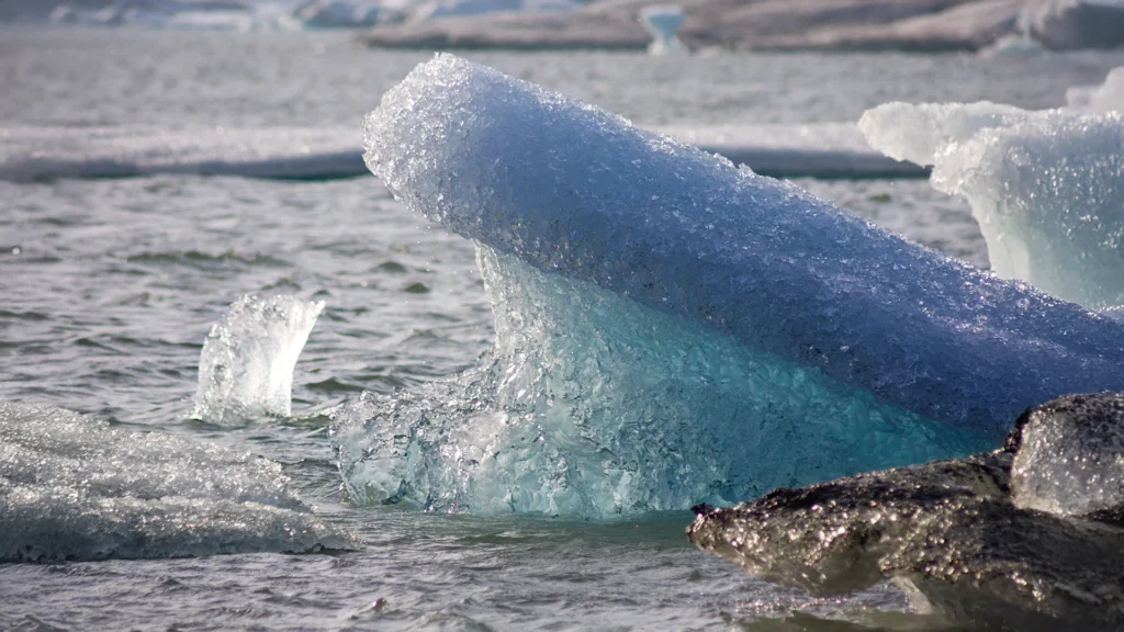 Primer plano de un iceberg azul turquesa flotando en una laguna glaciar de Islandia, rodeado de fragmentos de hielo blanco y oscuro.
