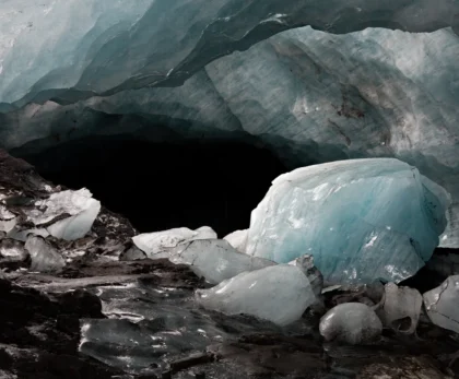 Interior de una cueva de hielo en Islandia con grandes bloques de hielo azul, paredes glaciares y sedimentos volcánicos oscuros.