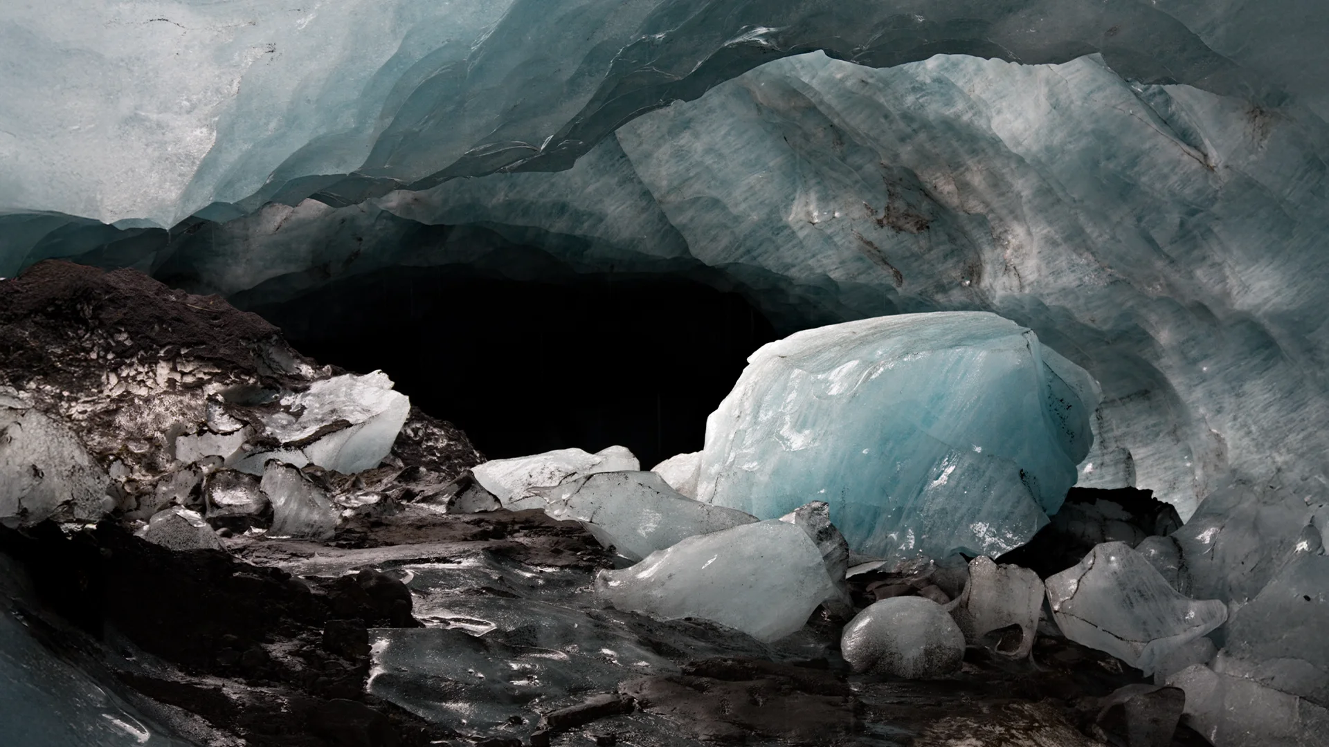 Interior de una cueva de hielo en Islandia con grandes bloques de hielo azul, paredes glaciares y sedimentos volcánicos oscuros.