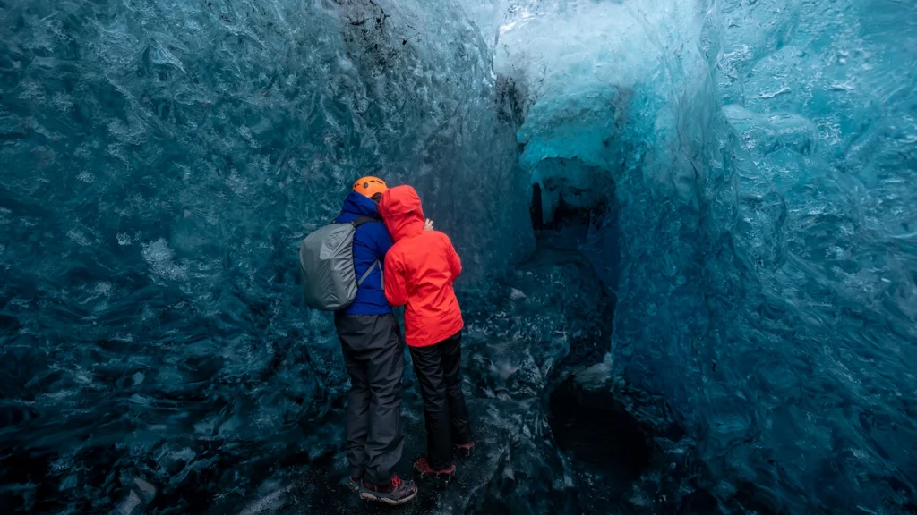 Dos visitantes con chaquetas de abrigo y cascos dentro de una cueva de hielo.